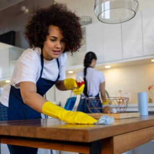 Professional Latin American cleaner cleaning a table at a house and smiling - housework concepts